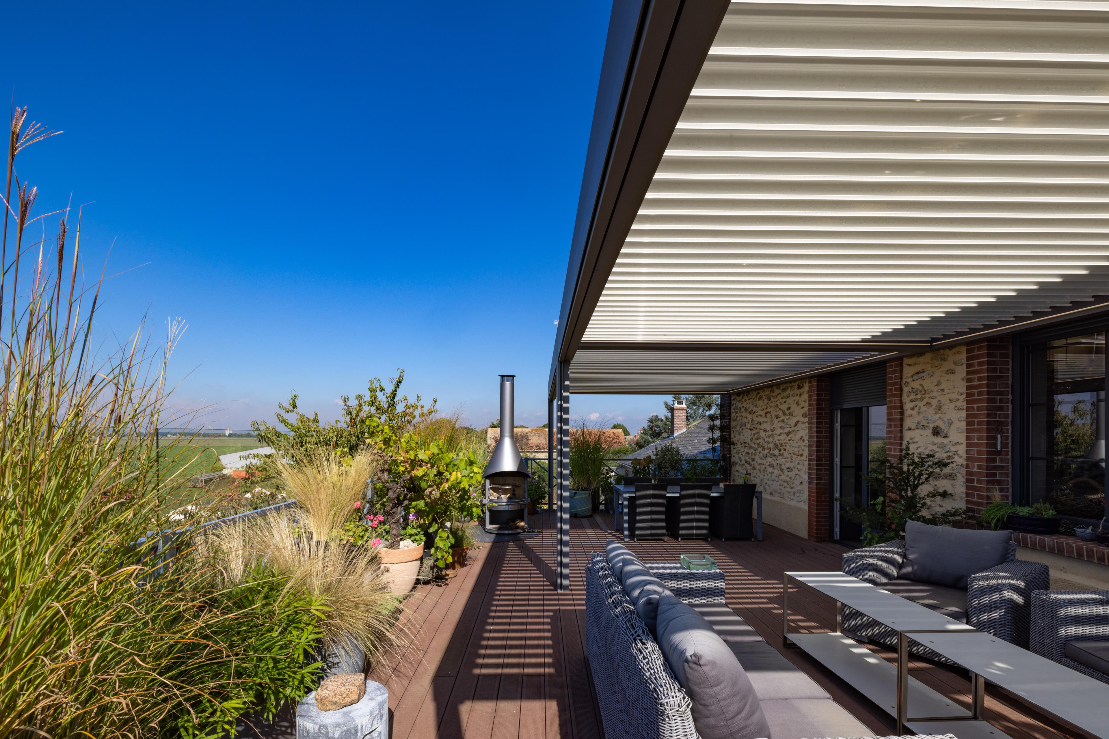 Pergola bioclimatique Biossun vue panoramique avec salon de jardin maison traditionnelle   